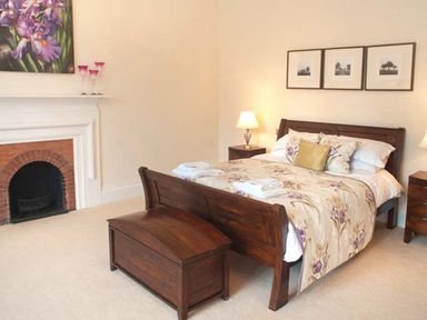 A bedroom with a wooden bed and bench a fireplace and framed pictures on the wall at The Hall in Belford
