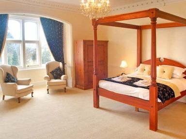 A bedroom with a four-poster bed two armchairs a wooden wardrobe and blue curtains at The Hall in Belford