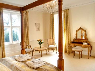 A bedroom with a four-poster bed towels on the bed two chairs a small table with flowers and a dressing table with a mirror at The Hall in Belford