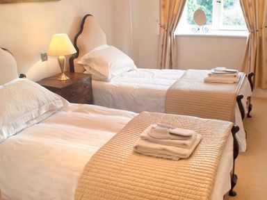 A bedroom with two single beds with beige bed runners and folded towels a wooden nightstand with a lamp and a window with curtains at The Hall in Belford