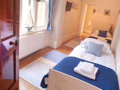 A bedroom with two single beds, white bedding, blue accents, a window with blue curtains, a wooden door, and a model sailboat on the windowsill at The Hall in Belford