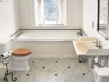 A bathroom with a bathtub under a window a toilet with a wooden seat and a wall-mounted sink at The Hall in Belford