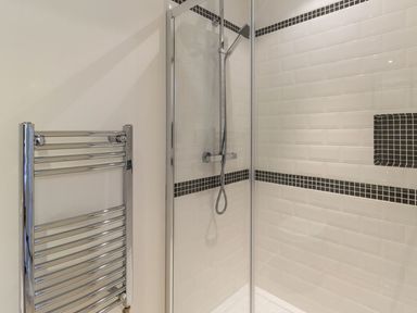 A shower area with glass door and black tile accents next to a chrome towel radiator at The Hall in Belford