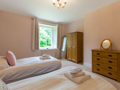 A bedroom with two single beds a wooden wardrobe a wooden dresser with a round mirror and a window with curtains at The Hall in Belford