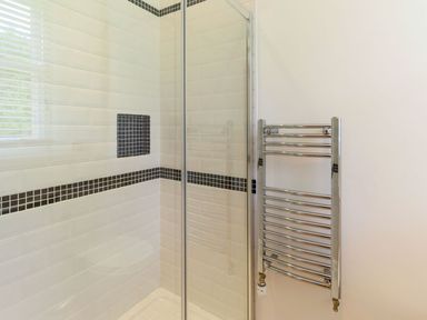 A shower area with glass door white tiles and black tile accents next to a chrome heated towel rail at The Hall in Belford