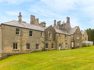 An exterior view of a large stone building with multiple chimneys and windows on a grassy slope at The Coach House in Belford