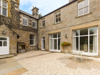 A stone courtyard with gravel and patio furniture outside a house with large windows at The Coach House in Belford