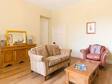 A living room with a striped sofa a leather armchair and wooden furniture at The Coach House in Belford