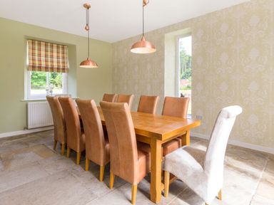 A dining room with a wooden table surrounded by brown chairs and one white chair at The Coach House in Belford