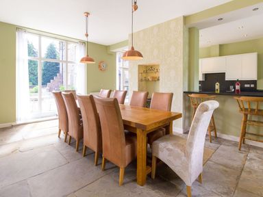 A dining room with a wooden table and ten chairs near large windows and a kitchen counter with bar stools at The Coach House in Belford