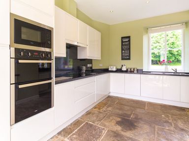 A kitchen with white cabinets black countertops a built in microwave and oven a window and a tiled floor at The Coach House in Belford