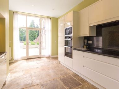A kitchen with white cabinets a black countertop built in oven and microwave and glass door leading outside at The Coach House in Belford