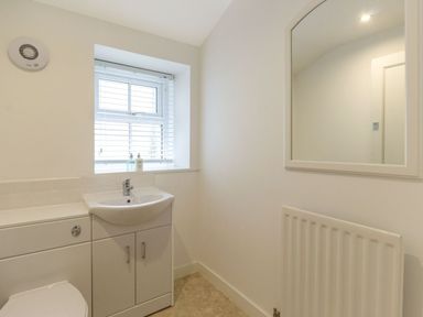 A bathroom with a sink, cabinet, toilet, window with blinds, mirror, radiator and a ventilation fan at The Coach House in Belford