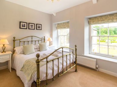 A bedroom with a metal frame bed two nightstands with lamps and windows showing a garden at The Coach House in Belford