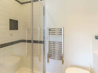 A bathroom with a glass shower enclosure tiled in white with black accent tiles and a chrome towel radiator at The Coach House in Belford