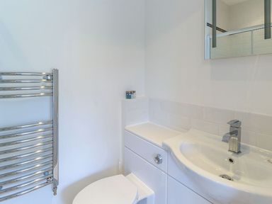 A bathroom with a white toilet a white sink with a silver faucet a wall-mounted mirror and a chrome towel radiator at The Coach House in Belford