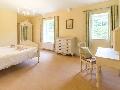 A bedroom with a bed dresser desk chair and windows with curtains at The Coach House in Belford