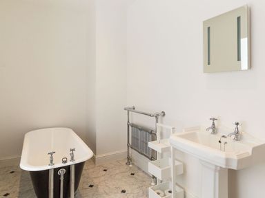 A bathroom with a freestanding bathtub a pedestal sink a wall-mounted mirror and a towel radiator at The Coach House in Belford