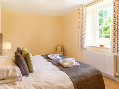 A bedroom with a bed with folded towels on it next to a window with patterned curtains at The Coach House in Belford