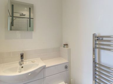 A bathroom with a sink and faucet a mirror a heated towel rail and toiletries on a shelf at The Coach House in Belford