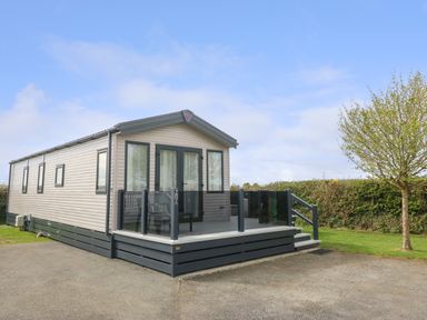 A mobile home with a small porch and glass railing next to a tree at Cornerstone Near Caernarfon