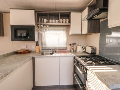 A kitchen with a microwave oven a gas stove a kettle toaster and a sink with mugs and wine glasses near a window at Cornerstone Near Caernarfon