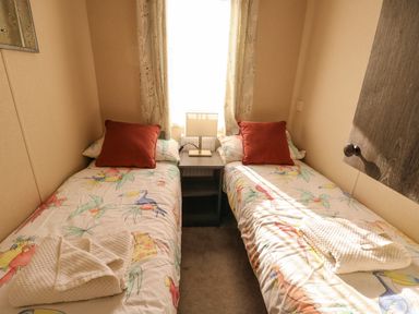 A small bedroom with two single beds with colorful bird patterned bedding and red pillows at Cornerstone Near Caernarfon