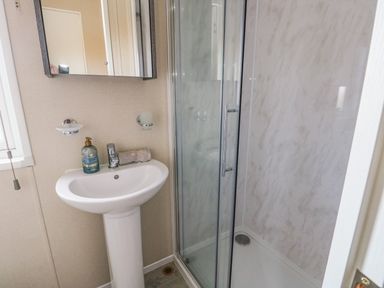A bathroom with a pedestal sink a mirror soap dispenser and a shower with glass doors at Cornerstone Near Caernarfon
