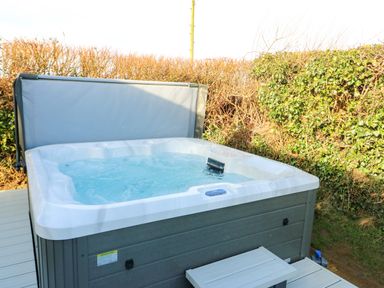 A hot tub with water and a cover partially open outside near hedges at Cornerstone Near Caernarfon