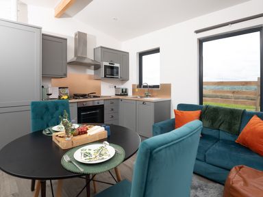A kitchen and dining area with grey cabinets a round black table set for two and a teal sofa with orange cushions at Cae Dafadd in New Mills near Llanfair Caereinion