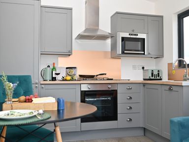 A kitchen with grey cabinets appliances and a dining table with food at Cae Dafadd in New Mills near Llanfair Caereinion