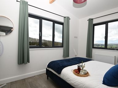 A bedroom with two windows green curtains a bed with a tray of tea and fruit at Cae Dafadd New Mills near Llanfair Caereinion