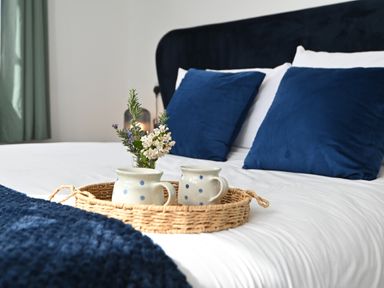 A bed with blue pillows and a wicker tray holding two mugs and flowers at Cae Dafadd in New Mills near Llanfair Caereinion