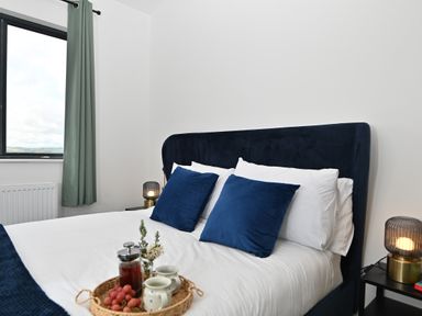 A bedroom with a bed having navy blue pillows and headboard with a tray of tea and grapes on the bed at Cae Dafadd in New Mills near Llanfair Caereinion