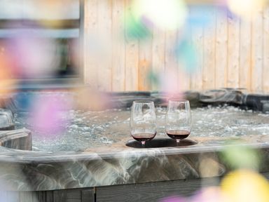Two glasses of red wine on the edge of a hot tub with wooden paneling in the background at Cae Bedw in Llanfair Caereinion