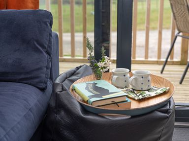 A wooden tray with two mugs flowers and a book on a black leather ottoman next to a blue sofa at Cae Bedw in Llanfair Caereinion