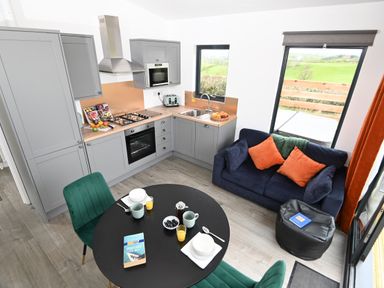 A kitchen with grey cabinets and a black oven next to a round black table with green chairs and a blue sofa with orange pillows at Cae Bedw in Llanfair Caereinion