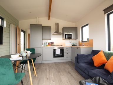 A kitchen and dining area with gray cabinets a black dining table with green chairs and a blue sofa with orange pillows at Cae Bedw in Llanfair Caereinion