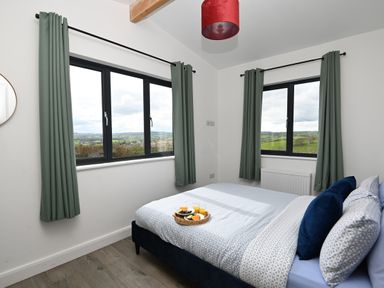 A bedroom with a double bed and windows showing countryside at Cae Bedw in Llanfair Caereinion