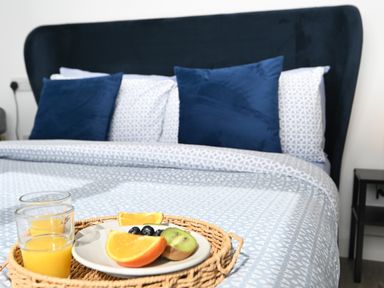 A bed with blue patterned bedding and blue pillows with a breakfast tray holding glasses of orange juice and a plate of fruit on the bed at Cae Bedw in Llanfair Caereinion