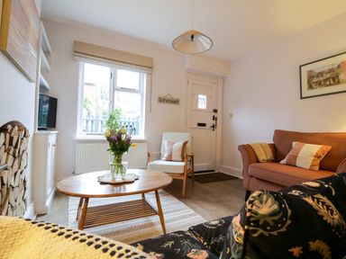 A living room with a wooden coffee table and flowers a sofa an armchair and a fireplace at Compass Cottage in Aldeburgh