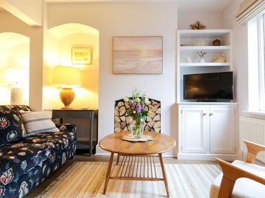 A living room with a floral sofa a wooden coffee table and a television at Compass Cottage in Aldeburgh