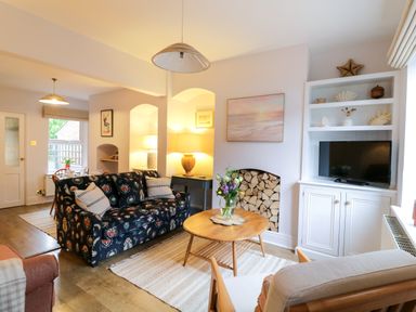 A living room with a floral sofa a wooden coffee table and a built in shelving unit with a television at Compass Cottage in Aldeburgh