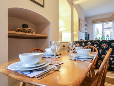A dining table set with white bowls and plates and wine glasses in a room with wooden chairs at Compass Cottage in Aldeburgh