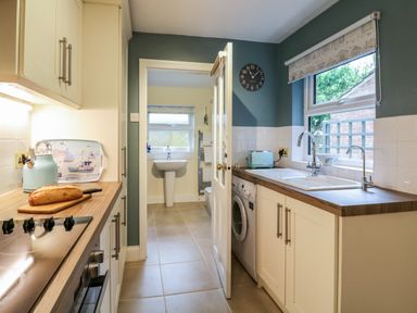 A kitchen with a loaf of bread on the counter a sink washing machine and a door leading to a bathroom at Compass Cottage in Aldeburgh