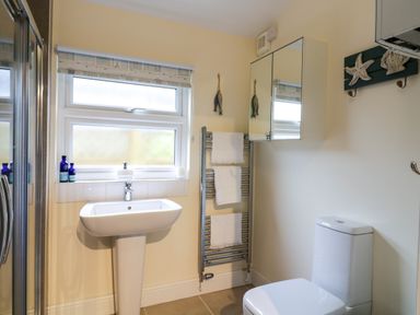 A bathroom with a white sink, toilet, towel rack with towels, mirrored cabinet, and a window at Compass Cottage in Aldeburgh