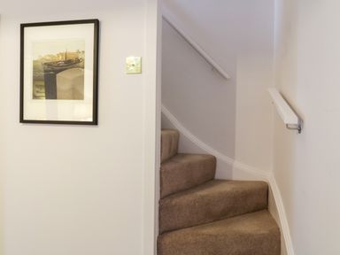 A narrow carpeted staircase with a handrail and a framed picture on the wall at Compass Cottage in Aldeburgh