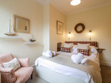 A bedroom with a double bed two wall lights and a patterned armchair at Compass Cottage in Aldeburgh