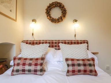 A bed with checkered and textured pillows and wall lights above at Compass Cottage in Aldeburgh