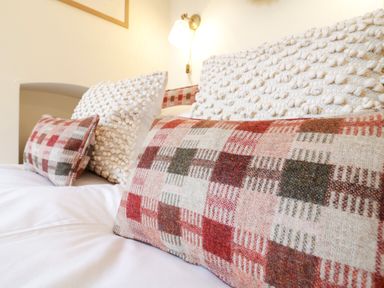 A bed with patterned and textured pillows in a bedroom at Compass Cottage in Aldeburgh